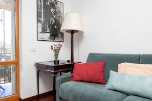 A room with a green sofa, a red pillow, a lamp, a framed picture, and a small table with a vase of flowers. - La Perla Rara | Stylish Apartment with Balcony Near Sorrento (SANT'AGNELLO)