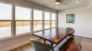 A dining area with a long wooden table, large windows, and a ceiling fan. - Waterfront NOLA Gem w/ Boat Dock & Lift on Wildlife Refuge (New Orleans)