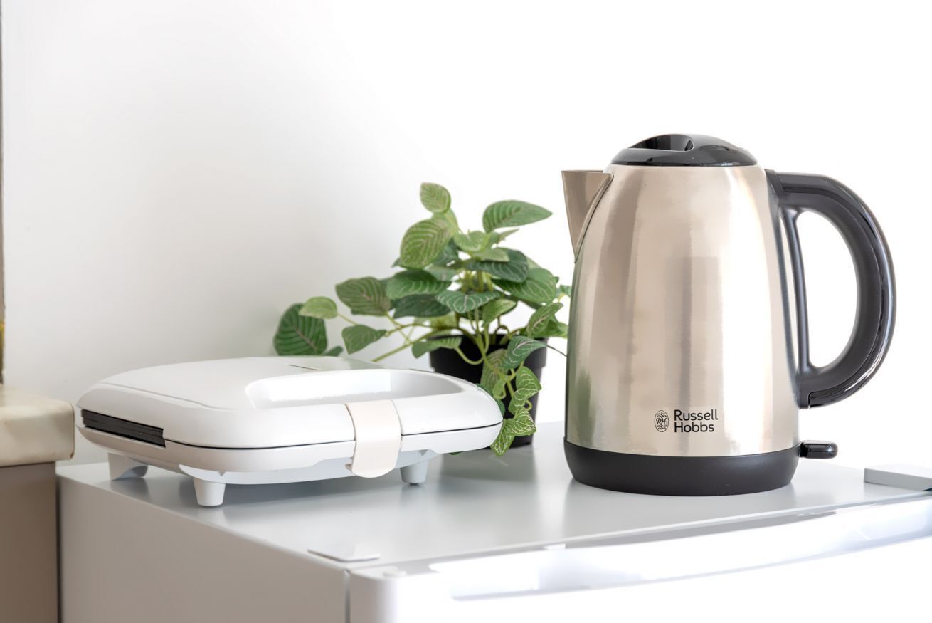 Une bouilloire électrique blanche et une cafetière en acier inoxydable de la marque Russell Hobbs, posées sur un plan de travail blanc.