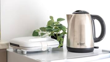 Une bouilloire électrique blanche et une cafetière en acier inoxydable de la marque Russell Hobbs, posées sur un plan de travail blanc.
