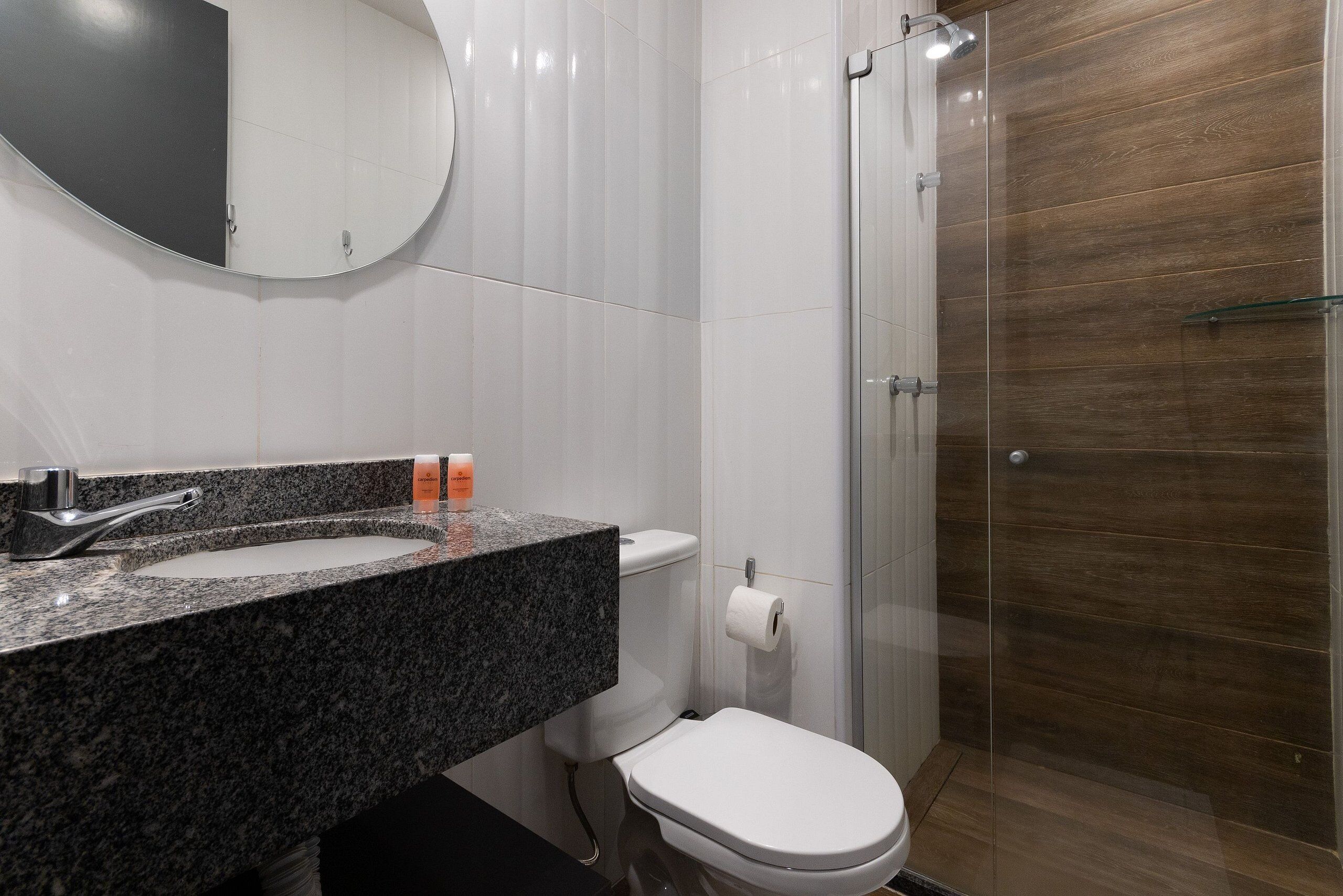 A modern bathroom with a granite countertop, white toilet, and a glass shower enclosure.