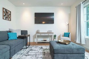 A modern living room with a grey sofa, a matching ottoman, a white armchair, and a console table with decorative items.
