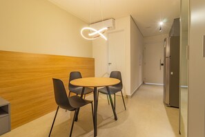 Ein modernes Hotelzimmer mit einer Wandpaneele aus Holz, einem runden Tisch mit vier Stühlen, einem Kühlschrank und einer Deckenleuchte.