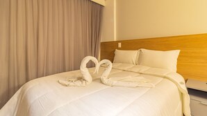 Ein Hotelzimmer mit einem ordentlich bezogenen Bett, einem Holzkopfteil und einem großen Fenster mit Vorhängen.