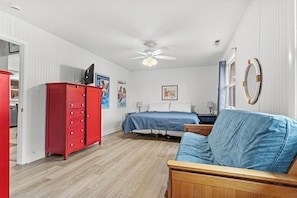 A bedroom with a bed, a red dresser, a blue sofa, and a ceiling fan.