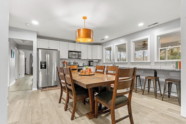 A modern kitchen with white cabinets, stainless steel appliances, a wooden dining table, and bar stools.