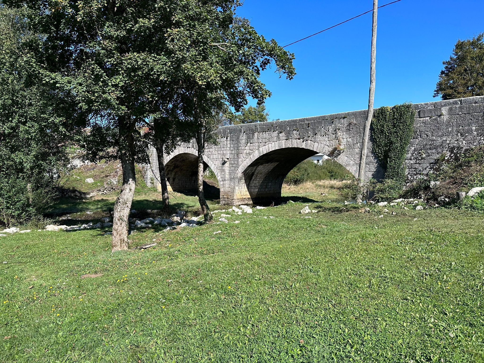 A stone bridge with two arches over a grassy area.