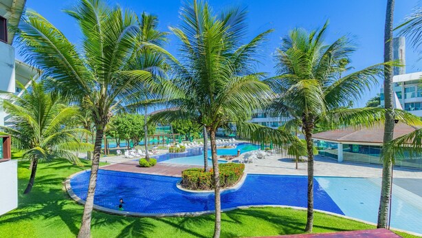 A pool area with palm trees, a circular pool, and lounge chairs. - Ancorar Resort #3103 - Beira Mar by Carpediem (Ipojuca)