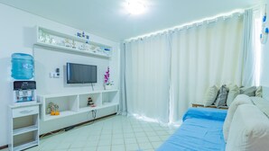 A bedroom with a bed, a TV on a stand, a water dispenser, and a shelf with decorative items. - Ancorar Resort #3103 - Beira Mar by Carpediem (Ipojuca)