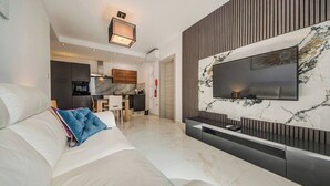 Un soggiorno moderno con un'ampia TV a schermo piatto montata su una parete in marmo, un divano con cuscini e un angolo cucina sullo sfondo.