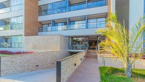 A modern building with multiple floors, large windows, and a pathway leading to the entrance. - Ora Beach #315 - Porto de Galinhas by Carpediem (Ipojuca)