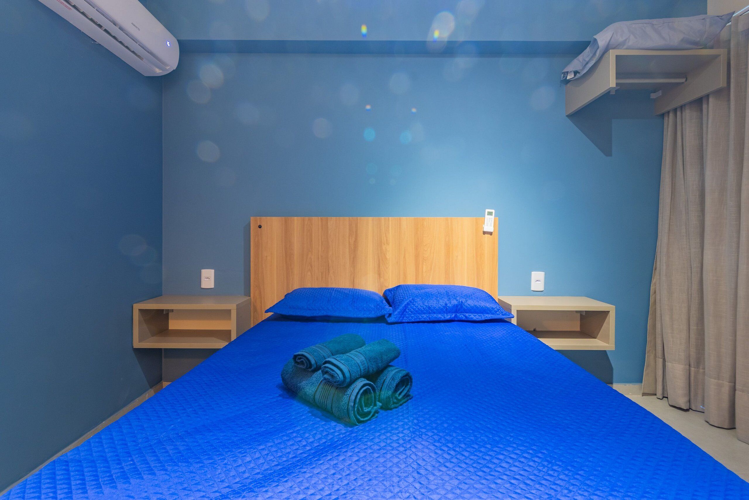 Une chambre avec un lit, deux tables de chevet, une tête de lit en bois et un mur bleu.