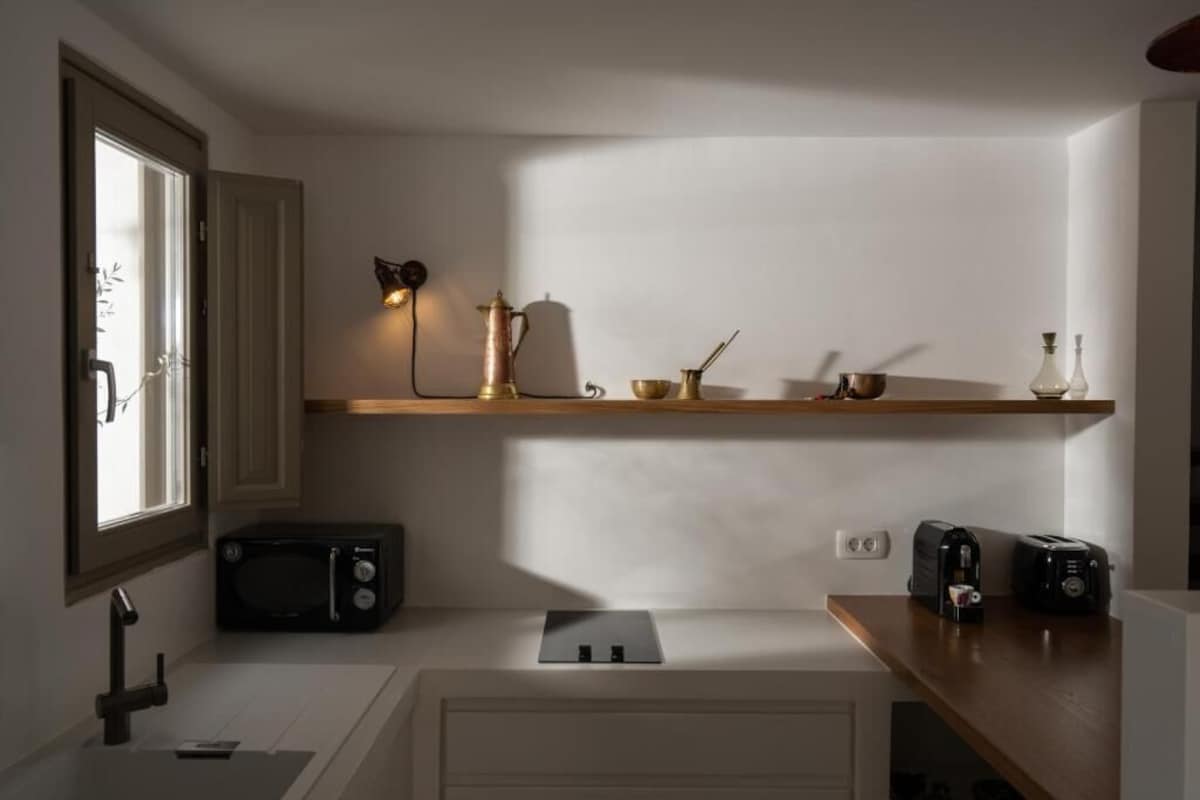A compact kitchen with a microwave, toaster, and shelf with kitchenware.