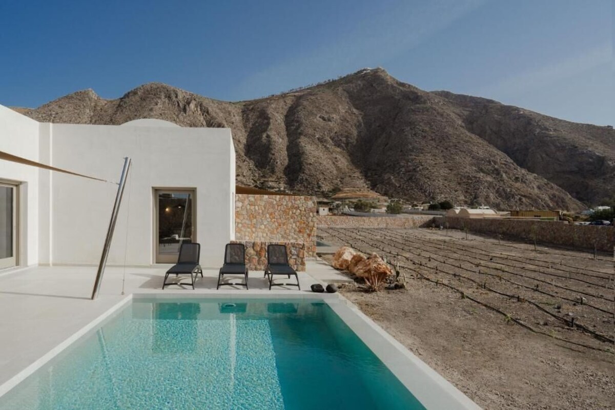 A pool area with a mountain backdrop, stone walls, and a few lounge chairs.