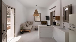A compact, modern kitchen with a central island, a built-in oven, and a flat-screen TV above the island. - Rizes Villas Santorini with private pool (Santorini)