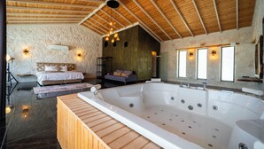 A spacious room with a large bathtub, a bed, a sofa, and a stone wall. - Villa Toprak (Kaş)