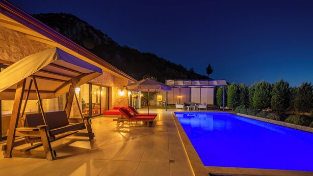 A pool area with lounge chairs and a covered seating area at dusk. - Villa Toprak (Kaş)