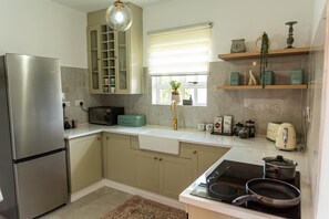 Una cocina moderna con un refrigerador de acero inoxidable, horno empotrado, un lavamanos y una estufa. Hay armarios, una ventana con persianas y un estante con utensilios de cocina.