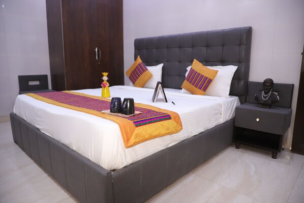 A neatly made bed with a grey headboard and white bedding, a bedside table with a statue, and a nightstand with a lamp.