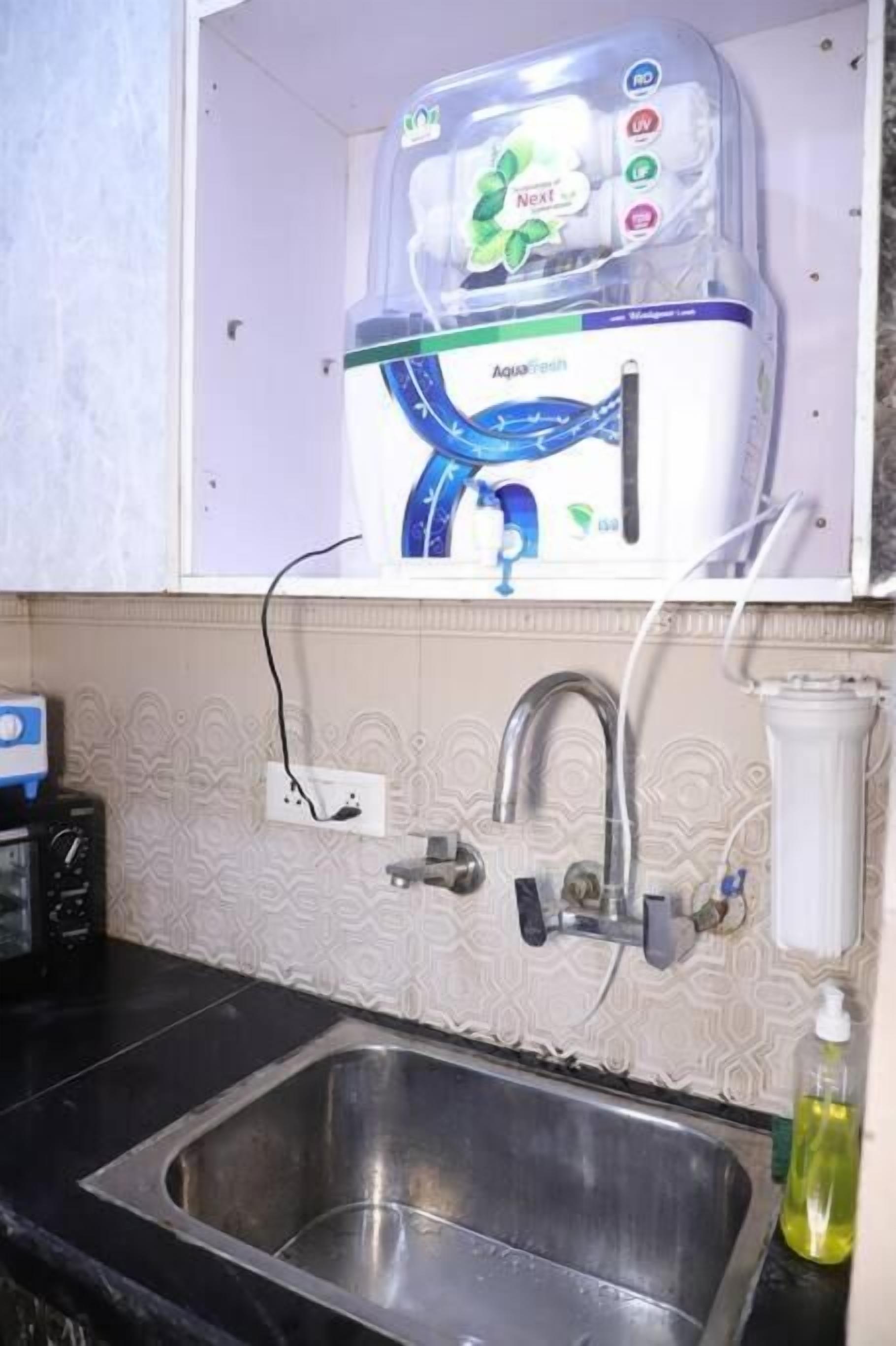 A kitchen with a stainless steel sink, a water filtration system, and a patterned backsplash.