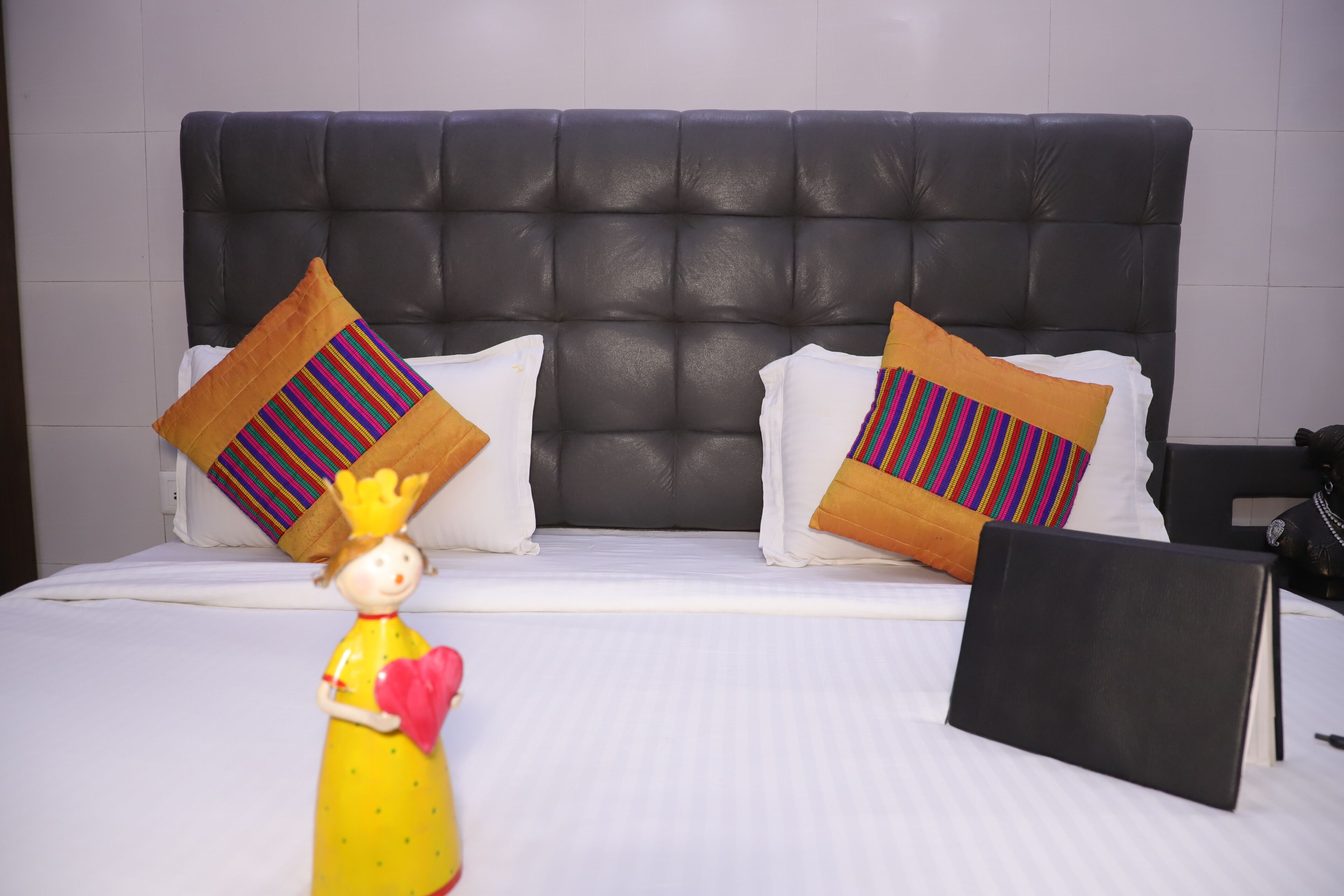 Ein Bett mit schwarzem Kopfteil, zwei Kissen mit Streifenmuster, eine kleine Figur und ein schwarzes Buch.