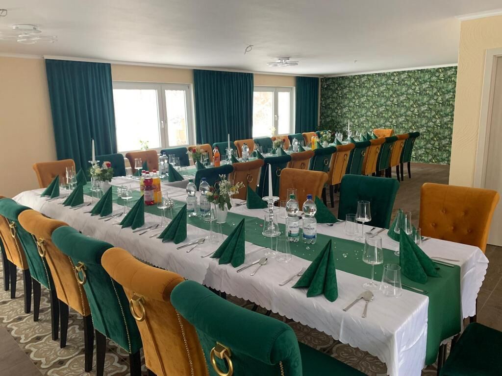 Un comedor con una mesa larga dispuesta para una comida, rodeada de sillas con tapicería verde y amarilla.