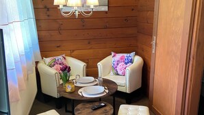 Ein gemütliches Blockhauszimmer mit Holzwänden, einem runden Esstisch mit weißen Stühlen, einer Kandelaber und einer großen Holztür.