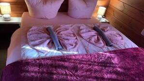 Ein ordentlich gemachtes Bett mit rosa Bettwäsche und zwei aufgerollten Handtüchern, einem hölzernen Kopfteil und Nachttischlampen.