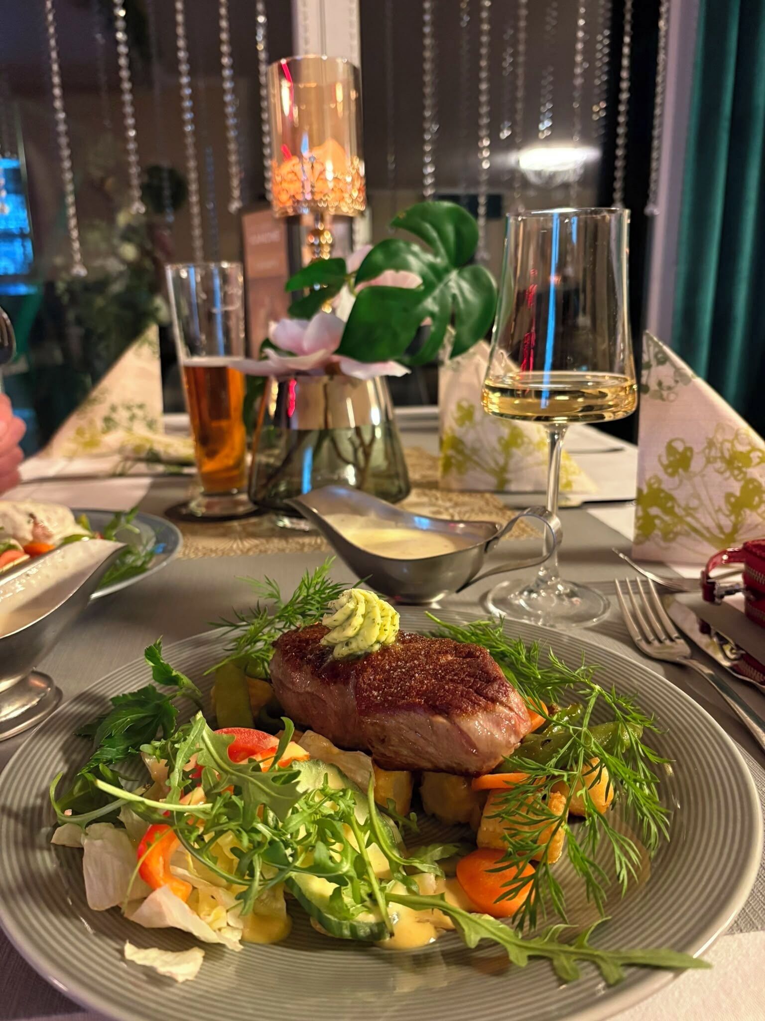 A dining table with a plate of food, a glass of white wine, and a glass of beer.