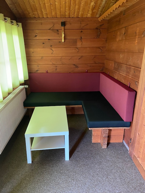 A wooden cabin interior with a green bench, a white table, and a radiator. - Naturpark Kanone (Markersdorf)