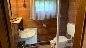 Ein kleines Badezimmer mit Holzvertäfelung, einem weißen Waschbecken, einer Toilette und einer Duschkabine.