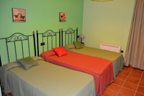 A room with two single beds, each with a different colored bedspread, a nightstand with a lamp, and a radiator. - Moriles Traditional Farmhouse for 8 (Moriles)