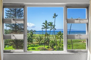 A window with a view of a tropical landscape including palm trees and a beach. - Beautiful Ocean View 2BR w/ Split AC & Private Lanai – Menehune Shores #524 (Kihei, Maui)