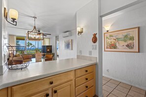 A kitchen with a large island, wooden cabinets, and a view of the ocean. - Beautiful Ocean View 2BR w/ Split AC & Private Lanai – Menehune Shores #524 (Kihei, Maui)