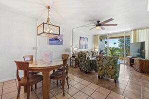 A spacious living area with a dining table, chairs, a sofa, and a television. - Beautiful Ocean View 2BR w/ Split AC & Private Lanai – Menehune Shores #524 (Kihei, Maui)