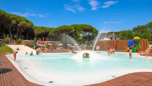 Ein Pool mit Wasserspielen, umgeben von Bäumen und einer Holzterrasse.