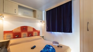 Ein Schlafzimmer mit Bett, Nachttisch, Fenster mit Vorhängen und einem Kopfstück mit Muster.