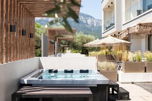A hot tub in an outdoor setting with wooden structures and wicker furniture. - Valen Mare Suites (Thasos)