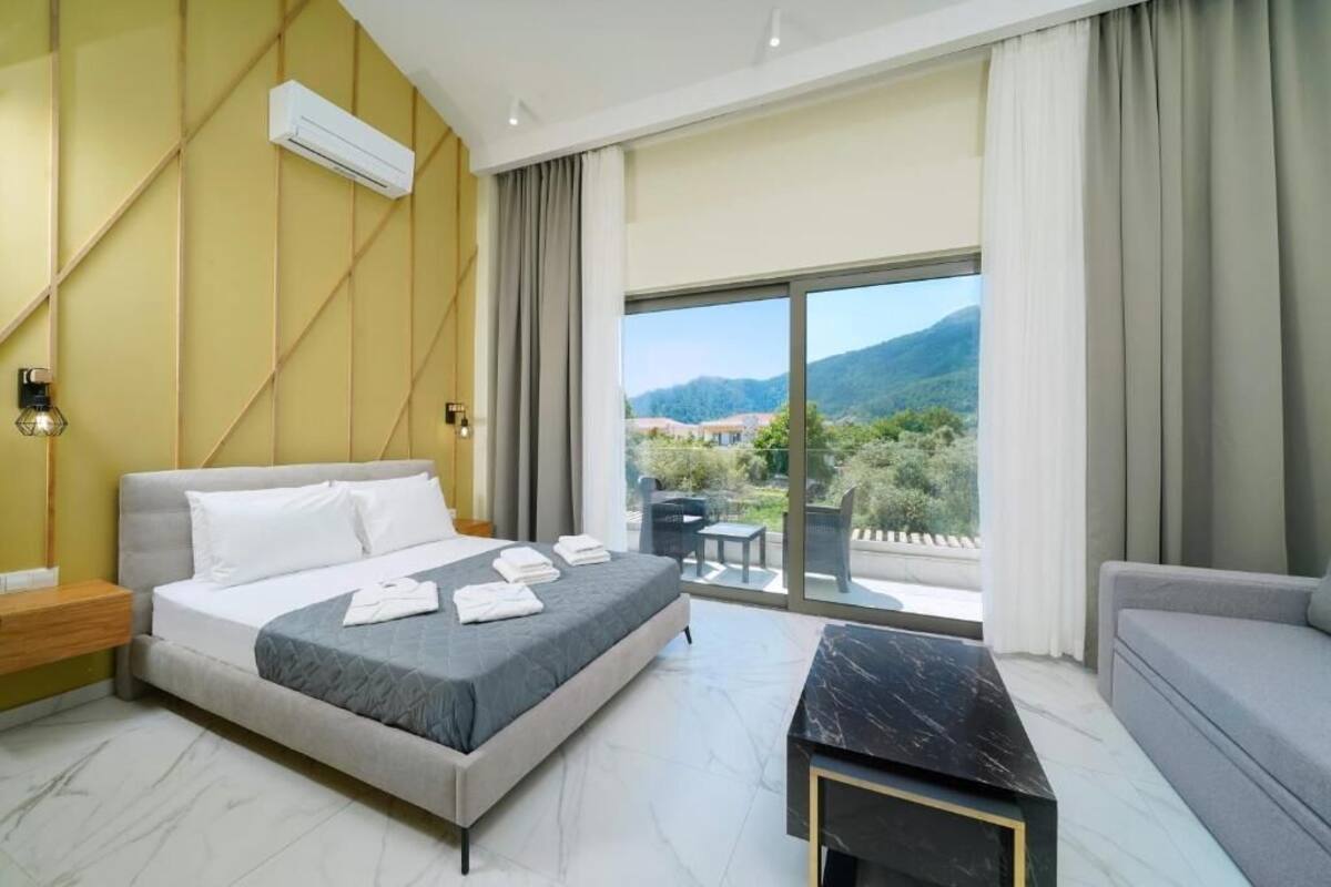 A modern hotel room with a large bed, a desk, and a balcony with a mountain view.