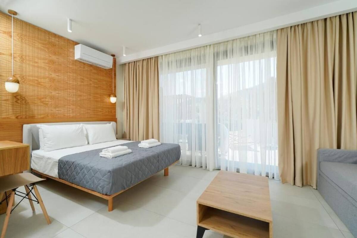 A modern hotel room with a bed, a desk, a sofa, and large windows with curtains.