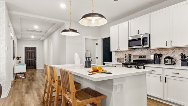 Una cocina moderna con armarios blancos, una isla central con taburetes de bar, microondas, estufa y cafetera.