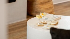 Un salón moderno con una mesa redonda blanca, dos vasos de una bebida amarilla y un libro titulado 'Minimalista'.