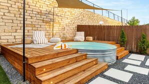 Una terraza de madera con jacuzzi, escalones y un muro de ladrillo.