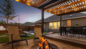 Un patio exterior con fogón, zona de estar y pérgola con guirnaldas de luces.