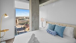 Quarto de hotel com uma cama grande, vista da cidade, um pilar de concreto e uma luminária moderna.