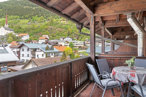 A balcony with a table and chairs, overlooking a village with houses and a church.