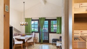 A dining area with a table, chairs, a chandelier, and a view through a window with curtains. - Apartment Azalea – Arrive, Feel at Home, Discover the Ötztal – Comfort in Central Oetz (Oetz)