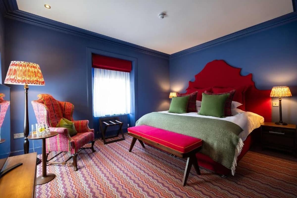 Una habitación de hotel con una cama grande, una silla, una mesita y un banco.
