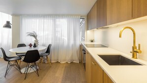 A modern kitchen with a white countertop, a gold faucet, and wooden cabinets. There is a dining area with a round table and black chairs. - Nordic Design with Sauna in Cental Helsinki (Kamppi) (Helsinki)