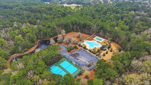 Vue aérienne d’un complexe hôtelier doté d’une piscine, de courts de tennis et d’une zone boisée naturelle.